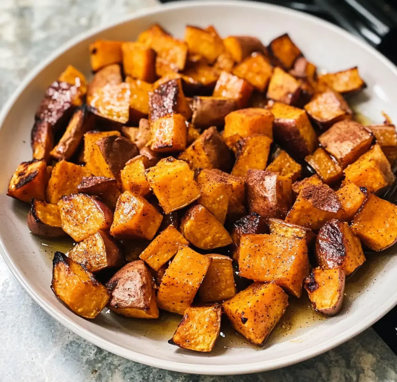 A plate of roasted, caramelized sweet potatoes cut into cubes and seasoned with spices.