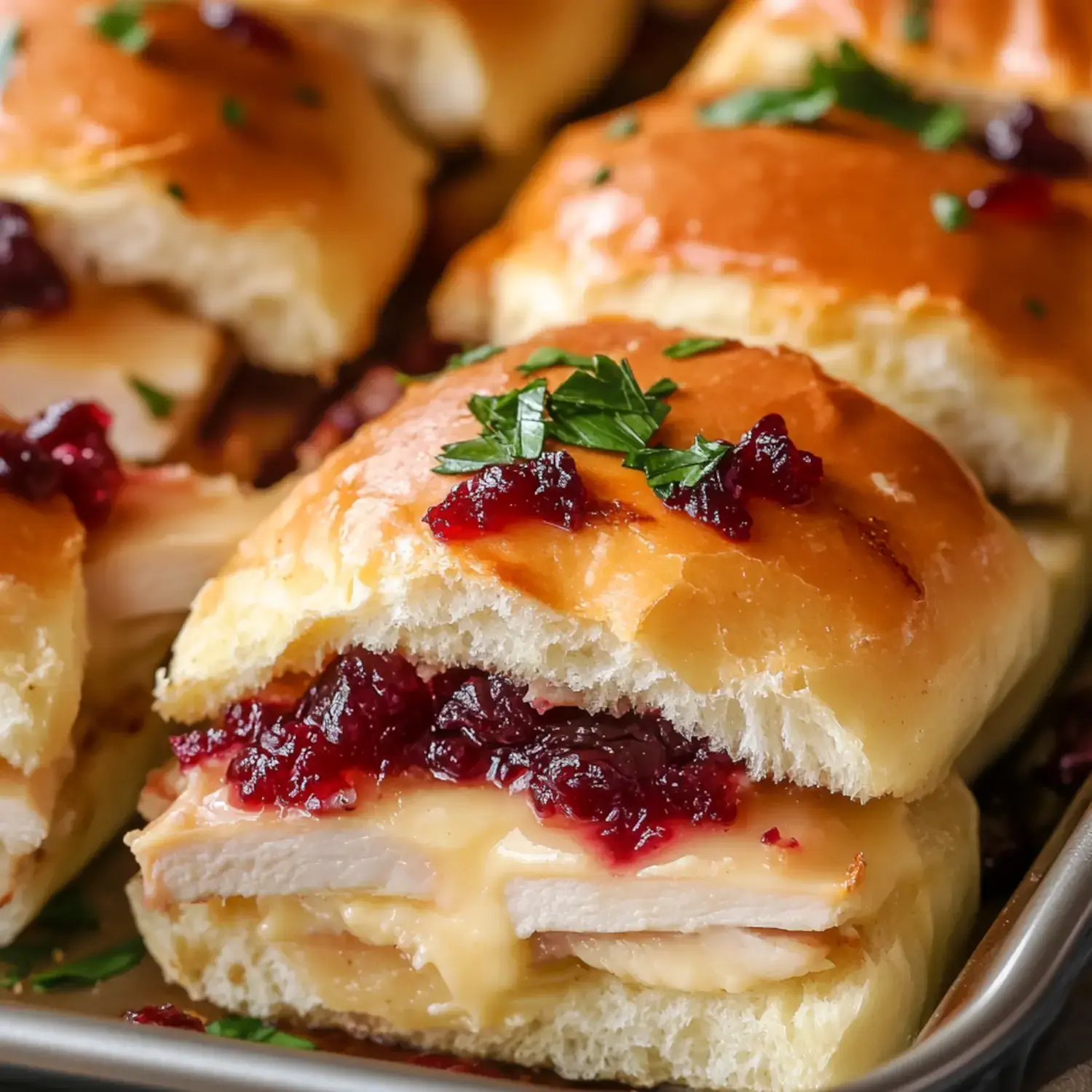 A close-up of a sandwich made with buttery bread, filled with turkey, melted cheese, and cranberry sauce, garnished with parsley.