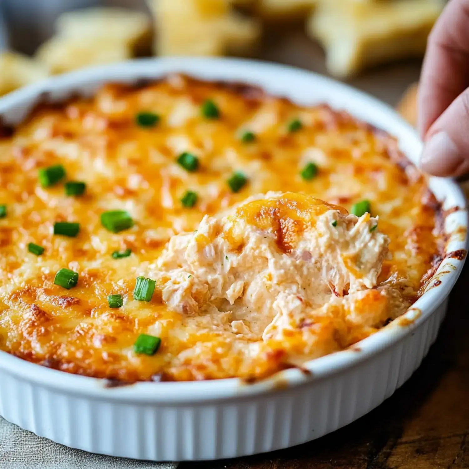 A cheesy, golden-brown dip is being served from a white baking dish, garnished with green onions.