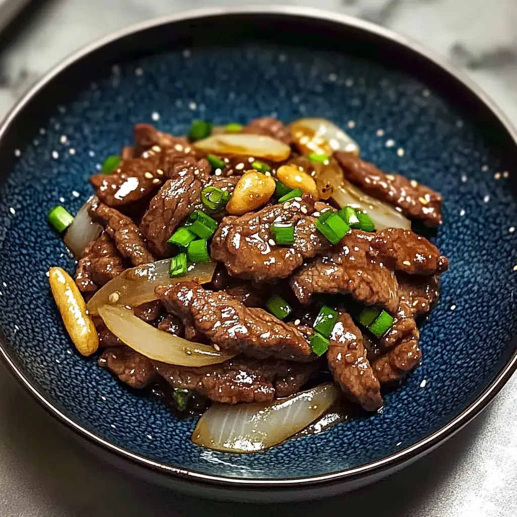 A close-up of a bowl filled with stir-fried beef, onions, and chopped green onions, garnished with sesame seeds and pine nuts.