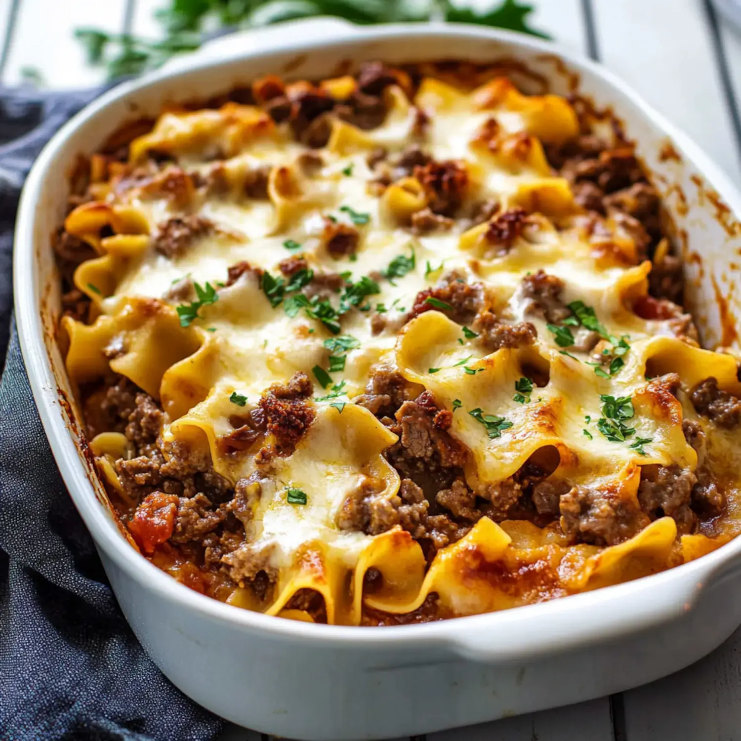 A baked dish of lasagna featuring layers of pasta, ground beef, and melted cheese, garnished with chopped parsley.