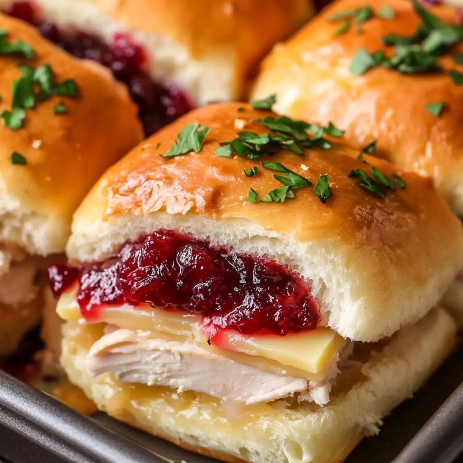 A close-up of a sandwich featuring sliced turkey, cheese, and cranberry sauce, served on a soft bun and garnished with parsley.