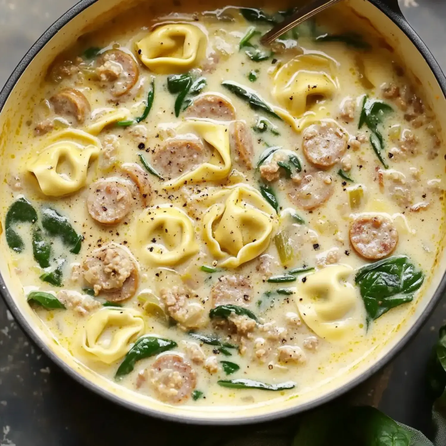 A creamy soup featuring tortellini, sausage, spinach, and spices, served in a bowl.