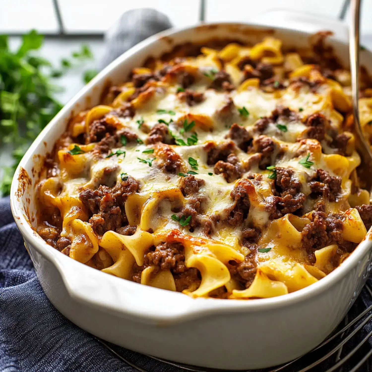 A baked casserole of egg noodles mixed with ground beef, topped with melted cheese and garnished with parsley.