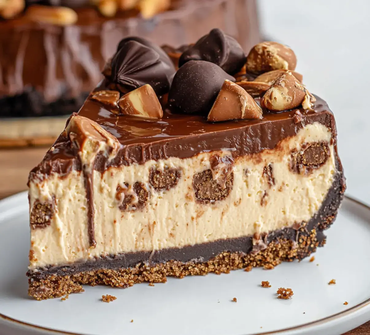 A slice of layered chocolate cheesecake, featuring a chocolate ganache topping, creamy filling with cookie pieces, and a graham cracker crust, garnished with chocolate candies.