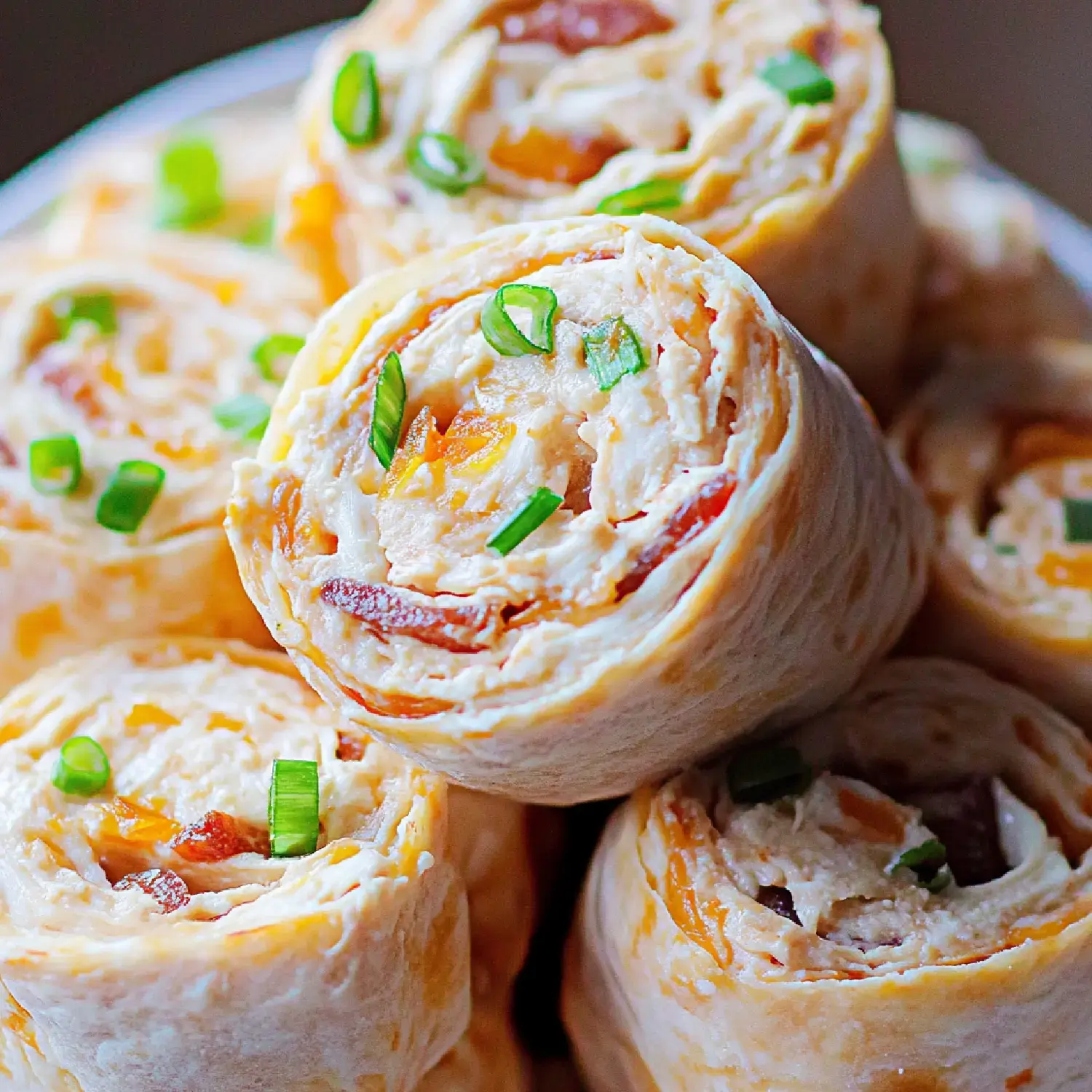 A close-up of a stack of rolled tortillas filled with cream cheese, bacon, and green onions, garnished with chopped green onions.