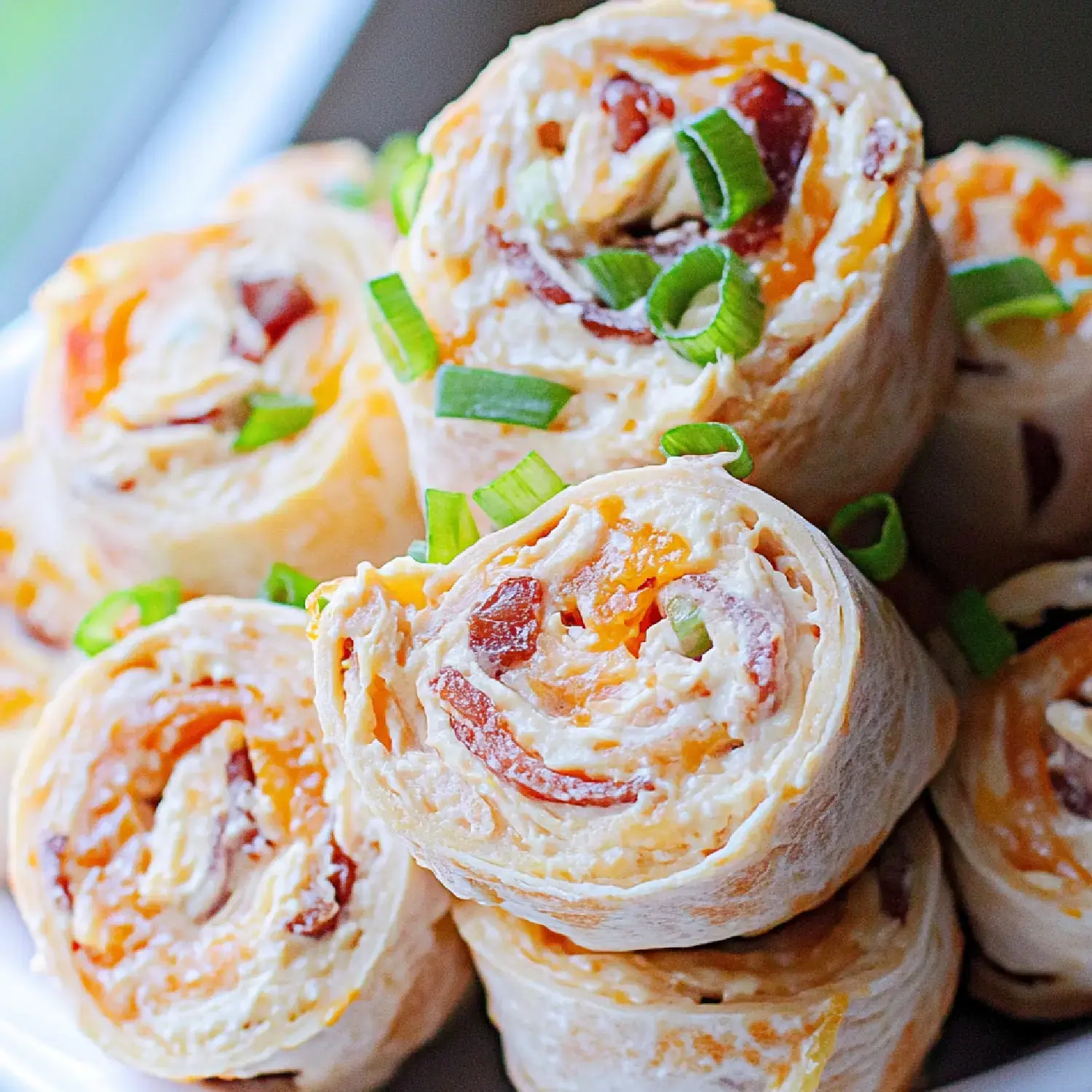 A close-up of sliced tortilla rolls filled with cream cheese, bacon, and cheese, garnished with green onions.