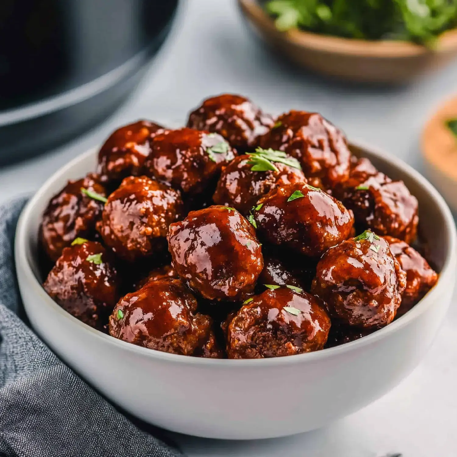 A bowl of glossy, brown sauce-coated meatballs garnished with fresh herbs.