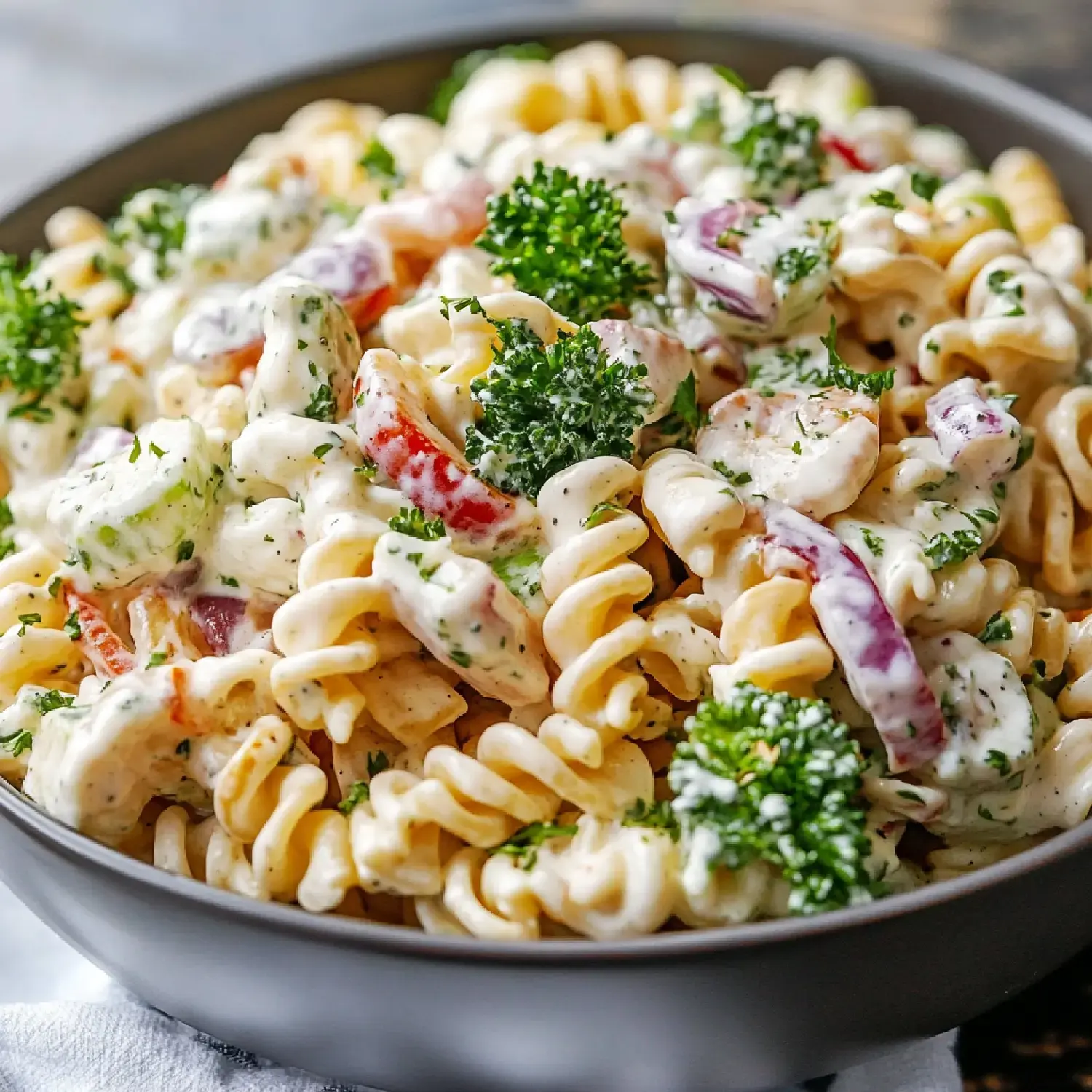 A close-up of a bowl filled with creamy pasta salad, featuring fusilli pasta, mixed vegetables, and garnished with parsley.