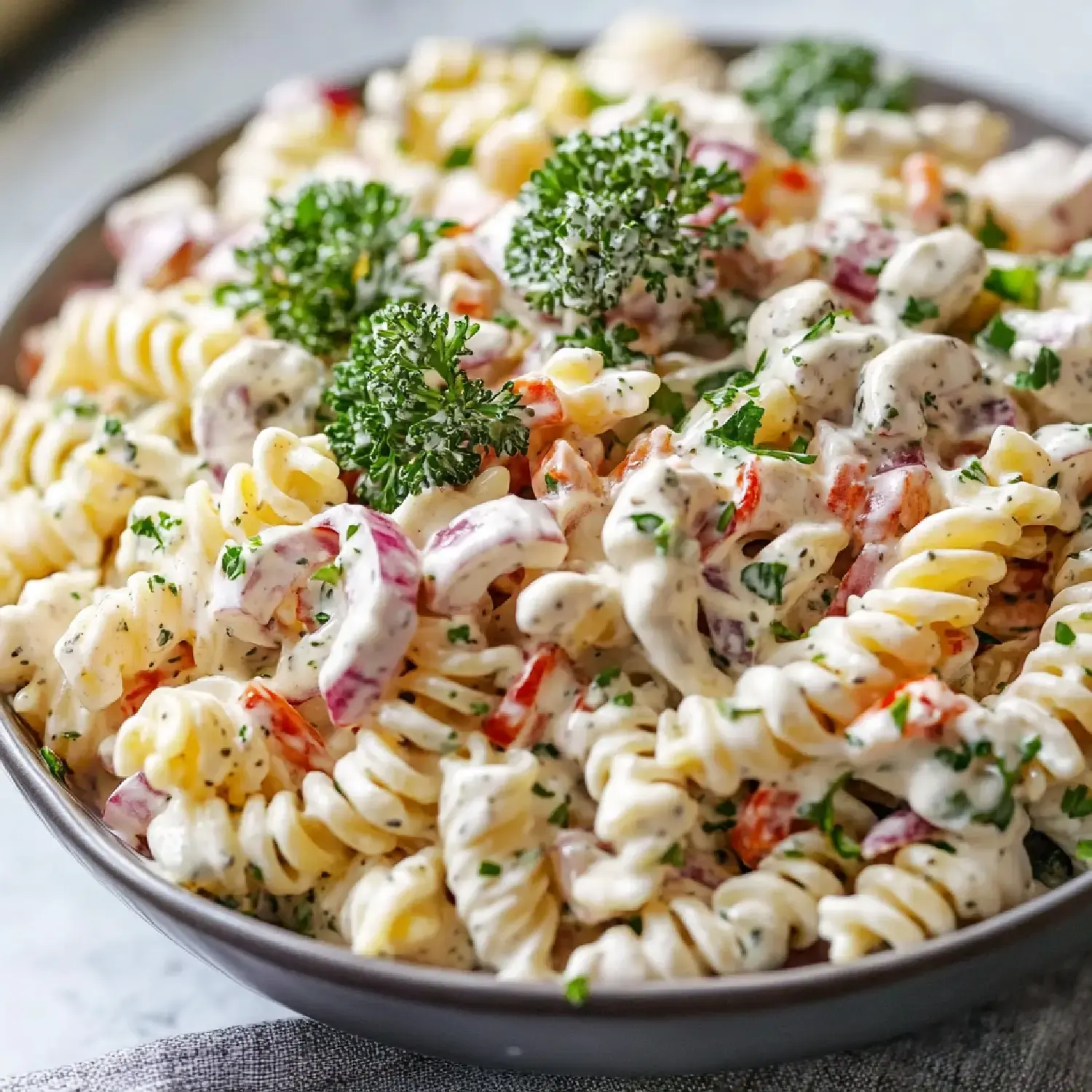 A close-up view of a bowl of creamy pasta salad mixed with colorful vegetables and garnished with fresh parsley.