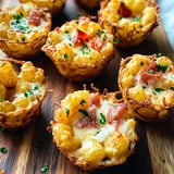 A close-up of crispy potato cups filled with cheese, bacon, and greenery on a wooden platter.