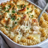 A creamy pasta dish with rotini, chicken pieces, and melted cheese, garnished with parsley.