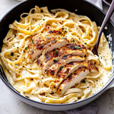 A bowl of fettuccine pasta coated in creamy sauce, topped with sliced grilled chicken and garnished with parsley.