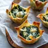 A platter of crispy pastry cups filled with a creamy spinach mixture sits on a wooden surface.